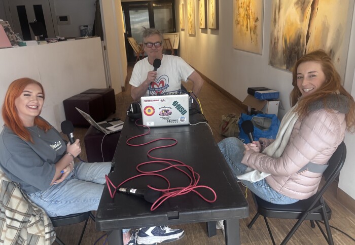 Two women and a man sitting around a table recording a podcast