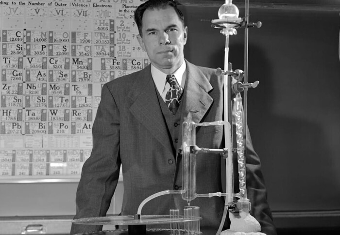 Glenn T. Seaborg in front of the periodic table with the ion exchanger elution column of actinide elements.