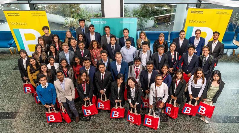 A group of student in the Imperial Business School building holding red IB tote bags